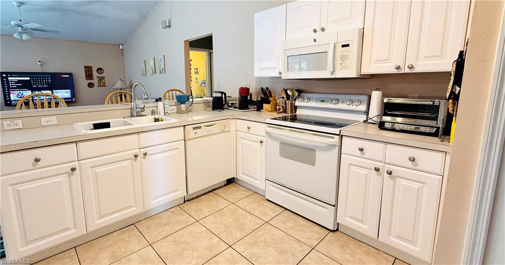Kitchen featuring white cabinetry, a double basin sink, white range, white dishwasher, and tile flooring