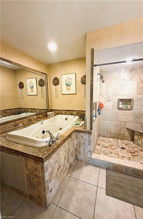 Jetted soaking tub with mosaic tile surround, walk-in shower with natural stone tiling, built-in shower bench, and a large wall mirror