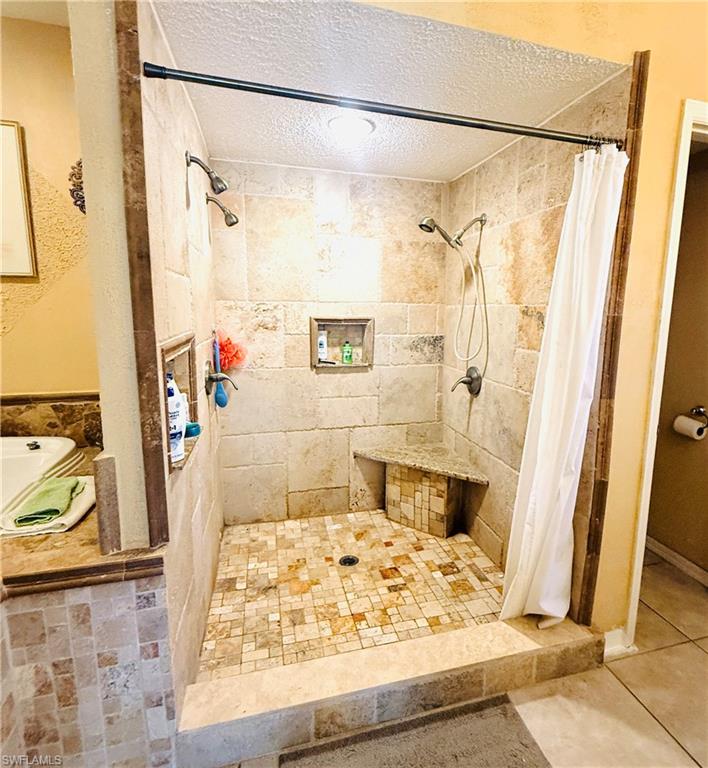 Tiled shower enclosure with dual shower heads, built-in bench seating, two recessed niches, and mosaic tile flooring