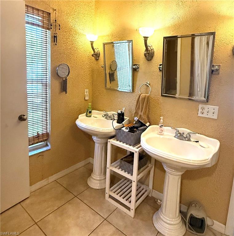 Pedestal sinks with individual mirrors, wall-mounted sconce lighting, and ceramic tile flooring