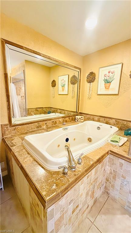 Built-in jetted tub with polished chrome fixtures, surrounded by a natural stone-finish countertop and mosaic tile accents