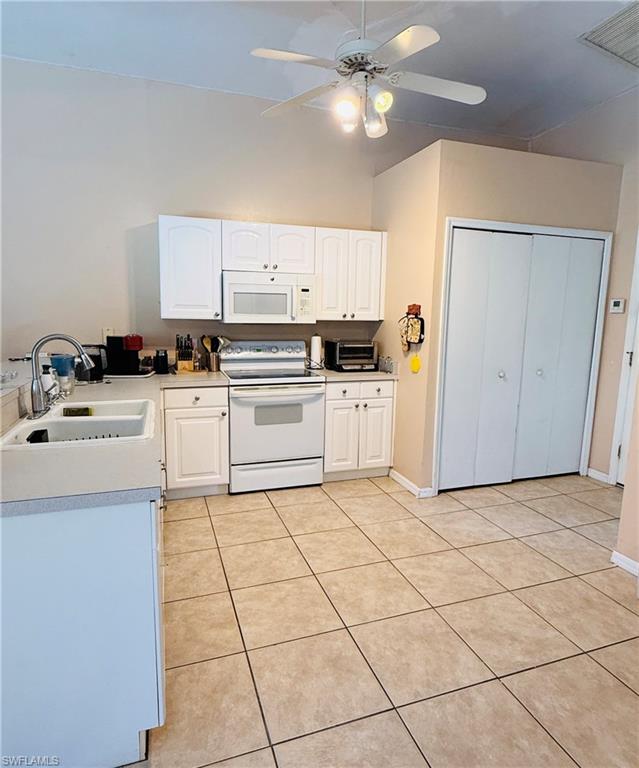 Kitchen featuring white cabinetry and appliances, tile flooring, a ceiling fan with integrated lighting, and a double-basin sink