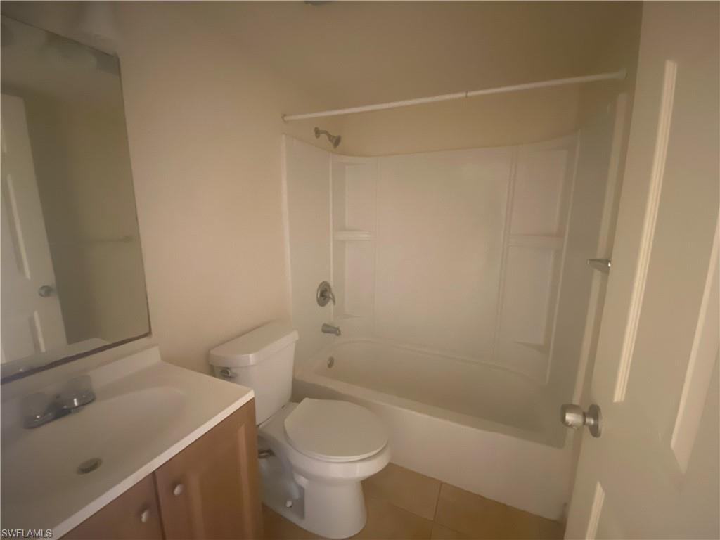 White shower/tub combination with built-in shelving, white toilet, vanity with wood-finish cabinetry, integrated sink, and chrome faucet