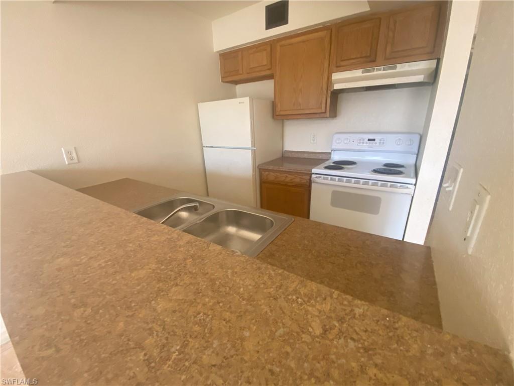 Kitchen featuring a double basin stainless steel sink, wood-finish cabinetry, white range, white refrigerator, and laminate countertops
