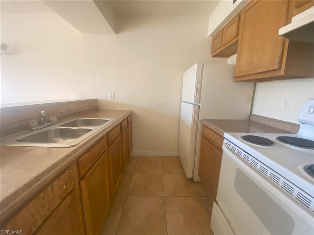 Kitchen featuring a dual basin sink, light-colored countertops, wood-finish cabinetry, and ceramic tile flooring
