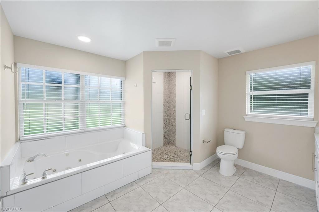 Spacious bathroom featuring a built-in jetted tub, a separate walk-in shower with glass enclosure, white tile flooring, and multiple windows