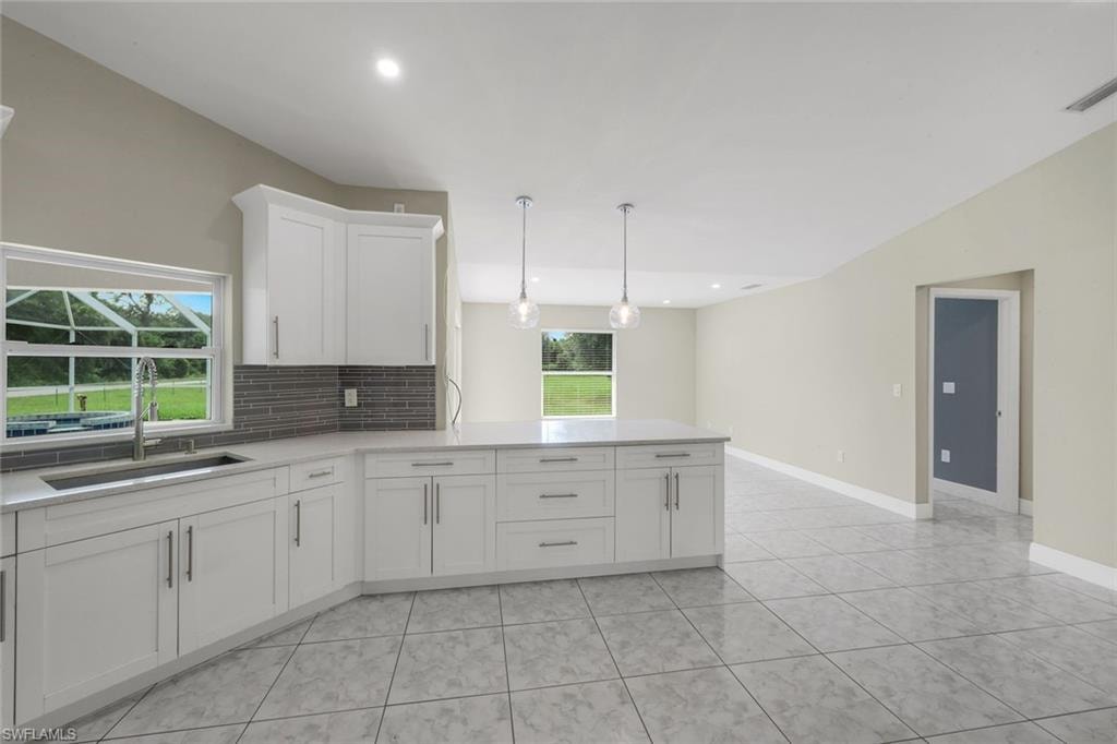 Kitchen featuring white cabinetry, grey subway tile backsplash, light-toned countertops, two pendant lights, and tile flooring