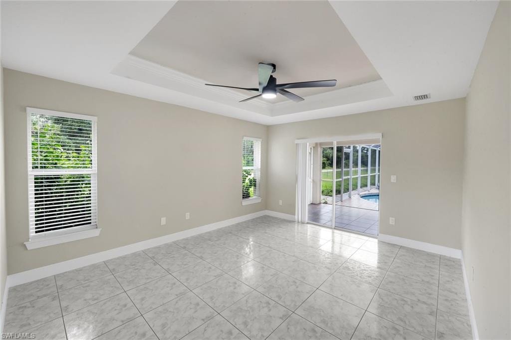 Spacious room featuring a tray ceiling, ceiling fan, and large windows