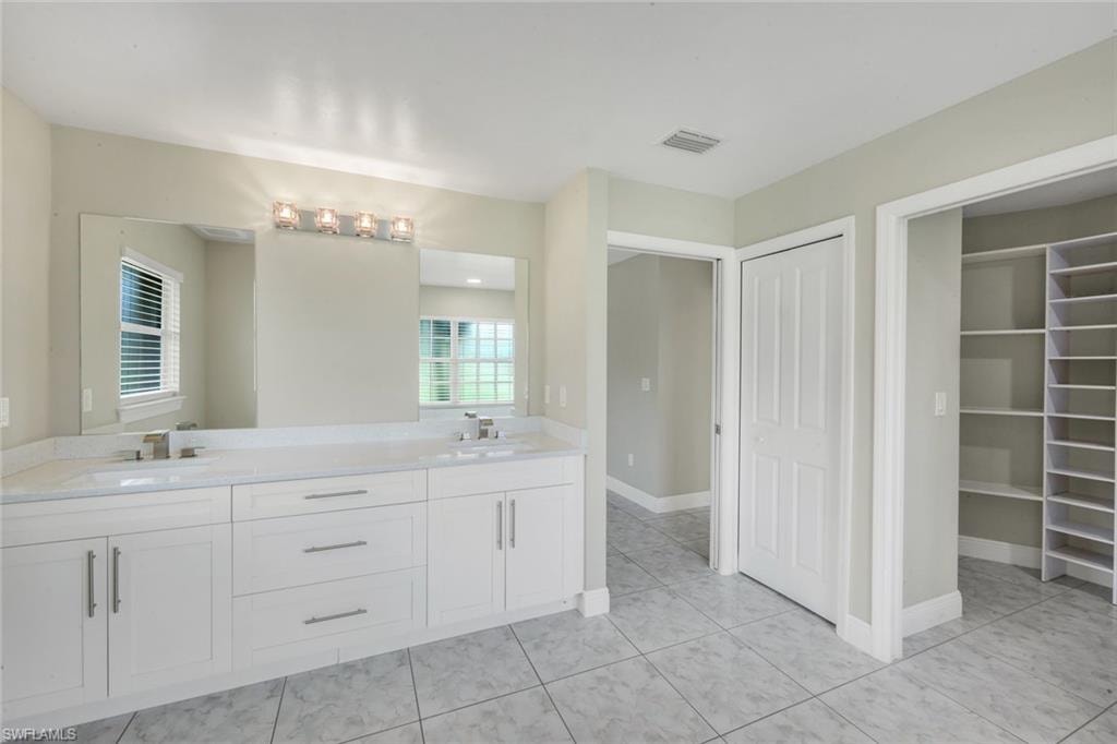 Dual vanity with stone countertop, large wall-mounted mirror, square tile flooring, built-in shelving, and white interior doors