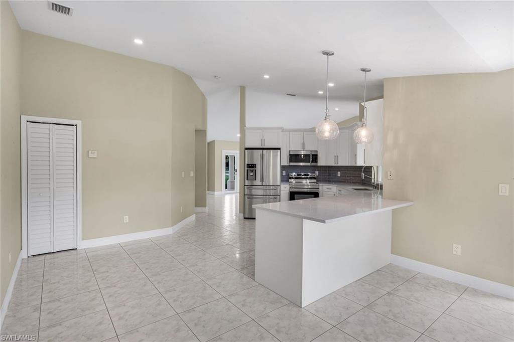 Open-concept living space featuring tiled flooring, vaulted ceilings, a kitchen island with seating, stainless steel appliances, and white cabinetry