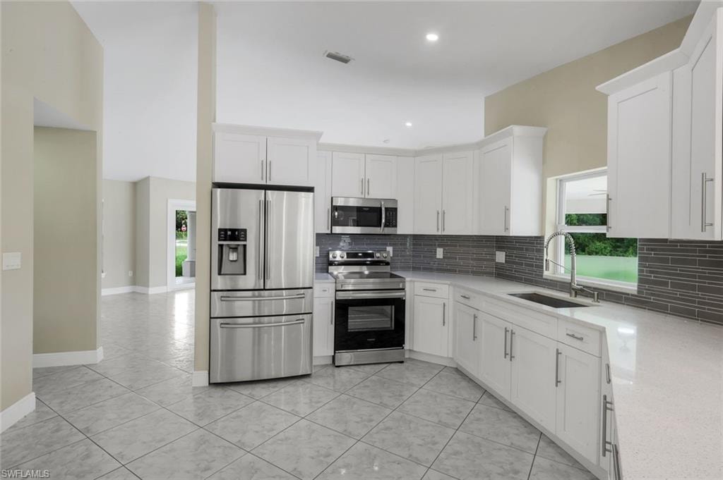 Kitchen featuring white cabinetry, stainless steel appliances, a grey tile backsplash, white countertops, and tile flooring