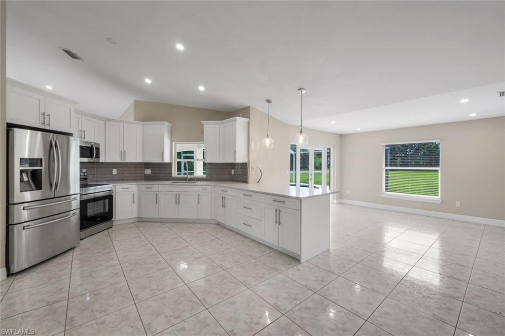 Open-concept kitchen featuring white cabinetry, stainless steel appliances, a center island with pendant lighting, and tile flooring
