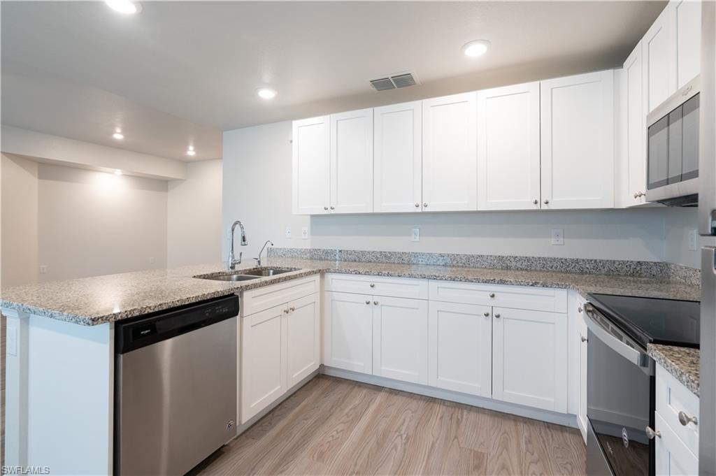 Kitchen featuring white shaker-style cabinetry, light wood-finish flooring, stainless steel appliances, speckled stone countertops, and recessed lighting