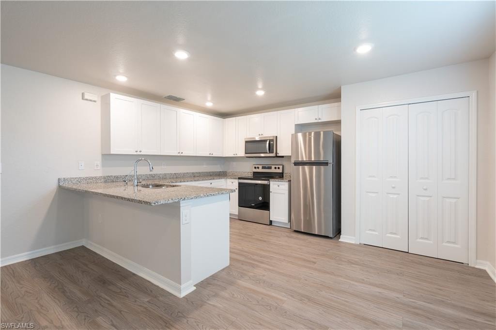 Kitchen with white cabinetry, granite countertops, stainless steel appliances, and wood-finish flooring