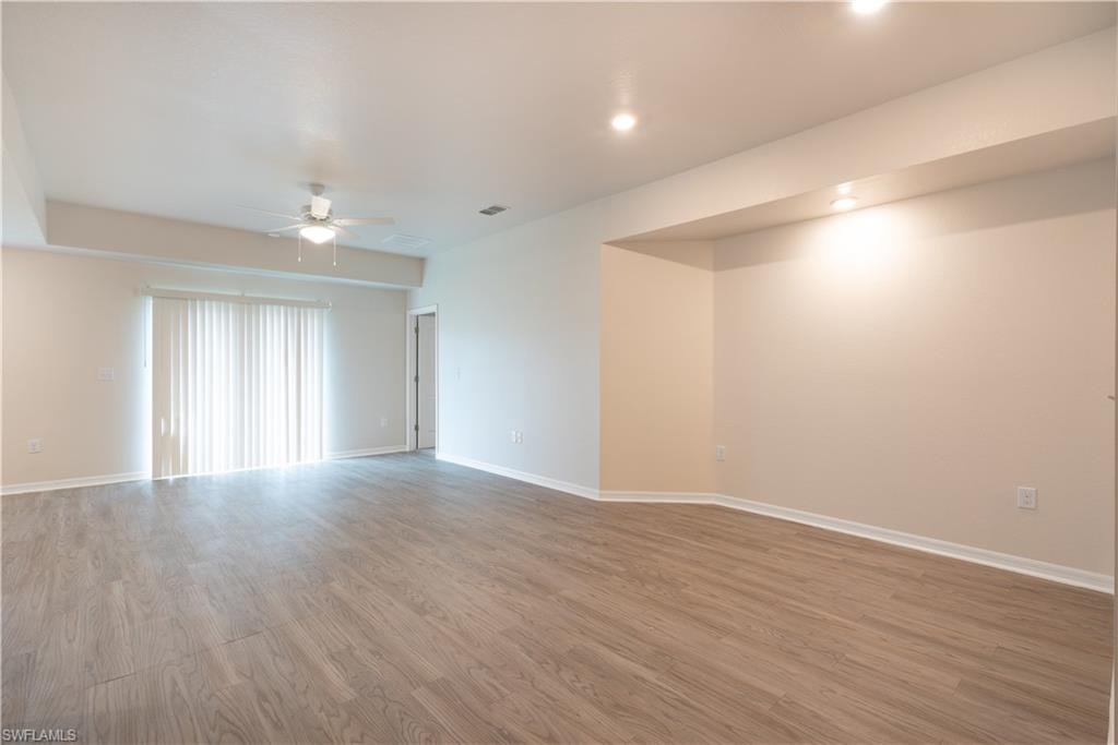 Spacious living area featuring wood-finish flooring, a ceiling fan, recessed lighting, and sliding glass doors with vertical blinds