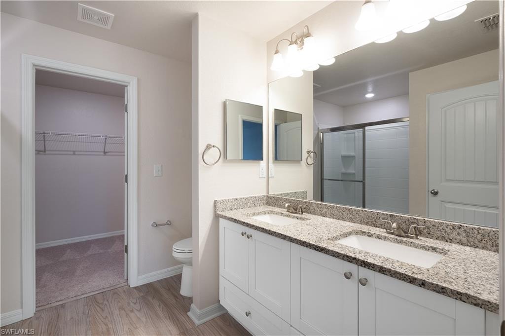 Double vanity with granite countertop, integrated sinks, chrome fixtures, and wood-finish flooring