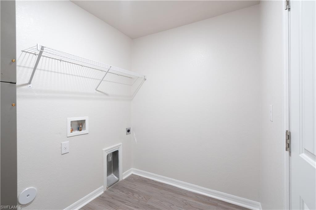 Dedicated laundry area with a wire shelf, utility hookups, and wood-finish flooring