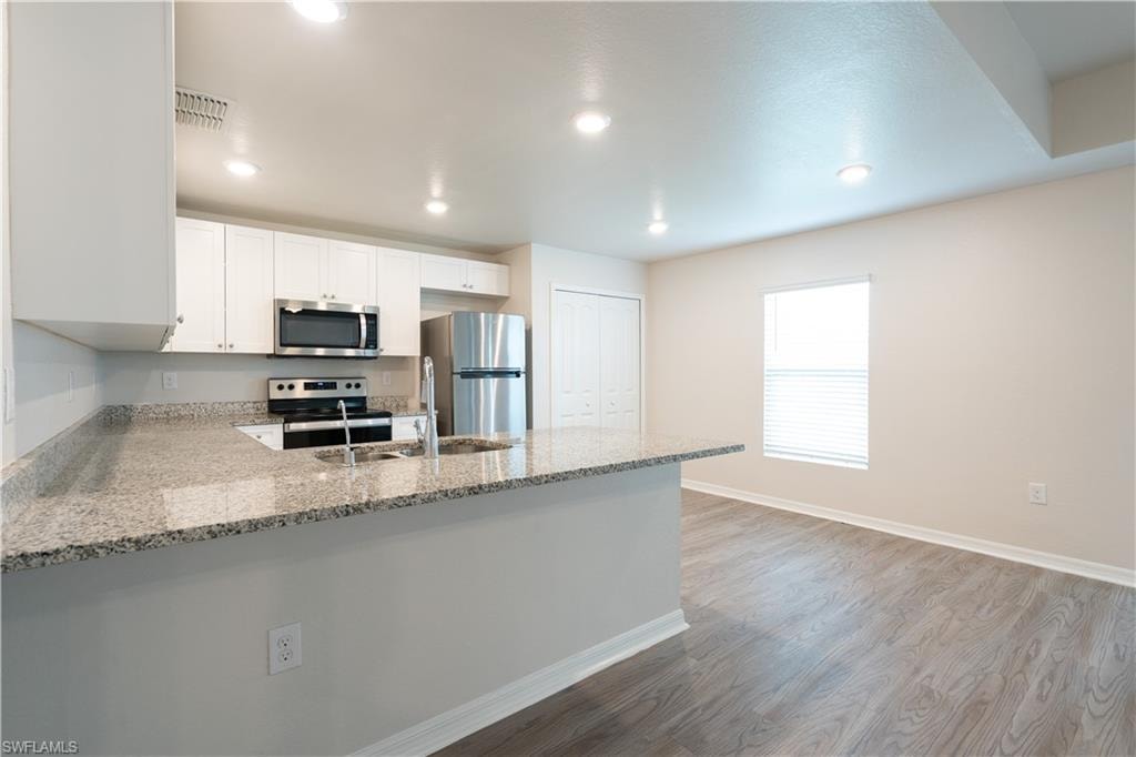 Kitchen with light wood-finish flooring, recessed lighting, white cabinetry, stainless steel appliances, and a granite-style countertop