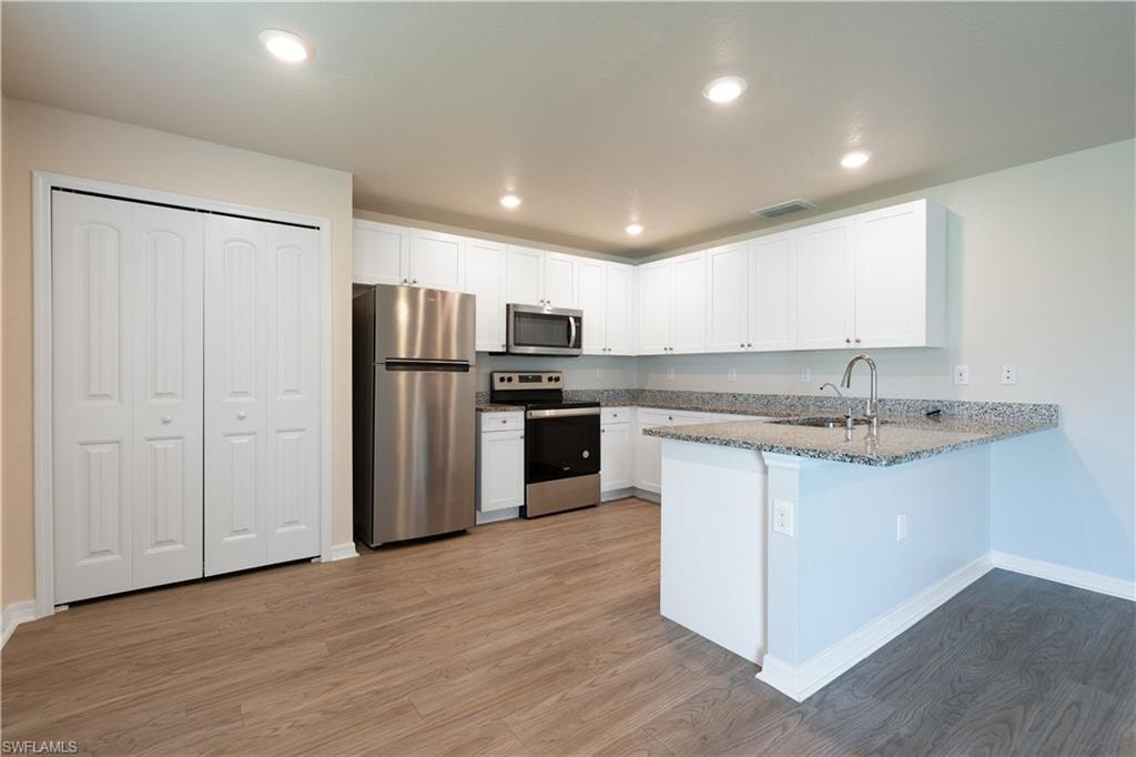 Kitchen featuring wood-finish flooring, white cabinetry, granite-style countertops, stainless steel appliances, and recessed lighting