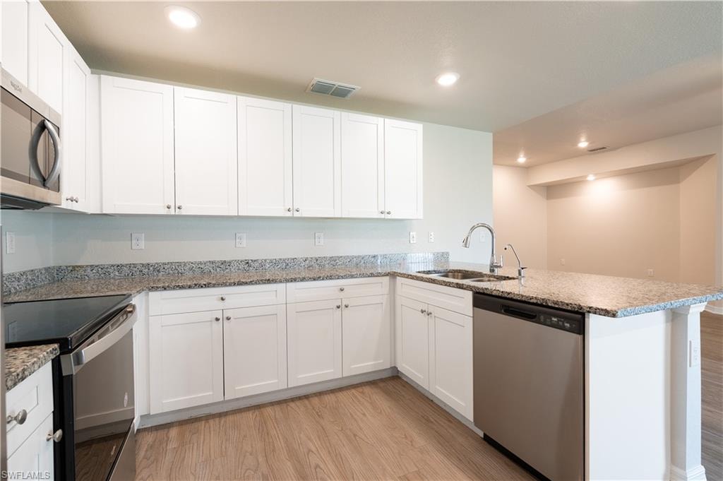 Kitchen featuring white cabinetry, granite countertops, wood-finish flooring, stainless steel appliances, and an undermount sink