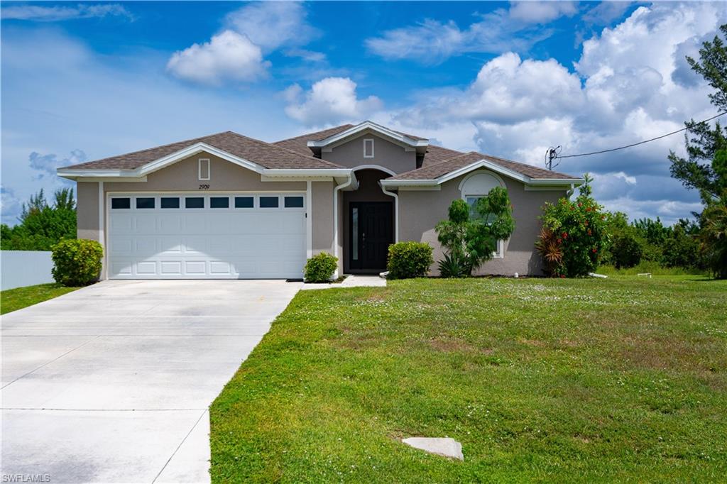 Stucco exterior with a hip roof, attached garage, concrete driveway, and front landscaping