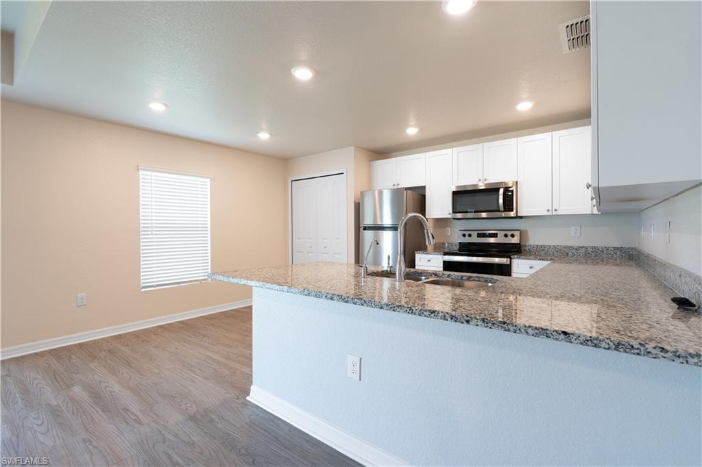 Kitchen featuring light-toned cabinetry, stainless steel appliances, speckled stone countertops, a single basin sink with a high-arch faucet, and recessed lighting