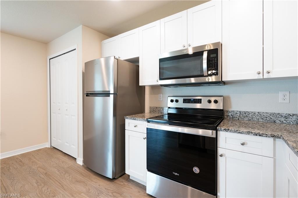 Wood-finish flooring, white cabinetry, stainless steel appliances, and granite countertops