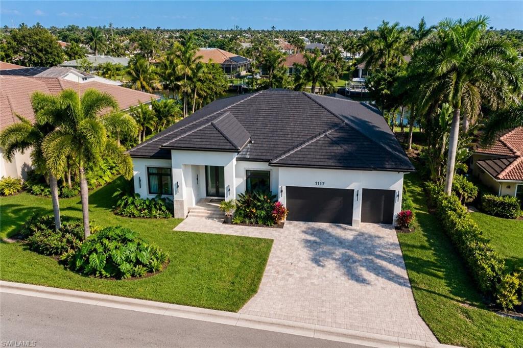 (Rendered photo) Exterior featuring a paver driveway, dark roof, and lush landscaping
