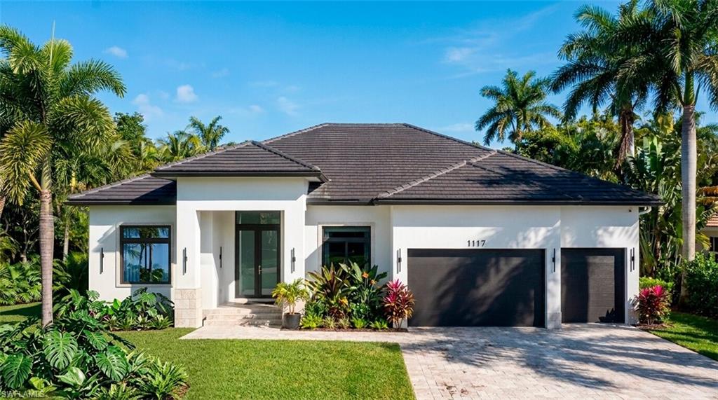 (Rendered photo) Contemporary stucco exterior with a dark tile roof, paved driveway, two dark garage doors, and lush tropical landscaping