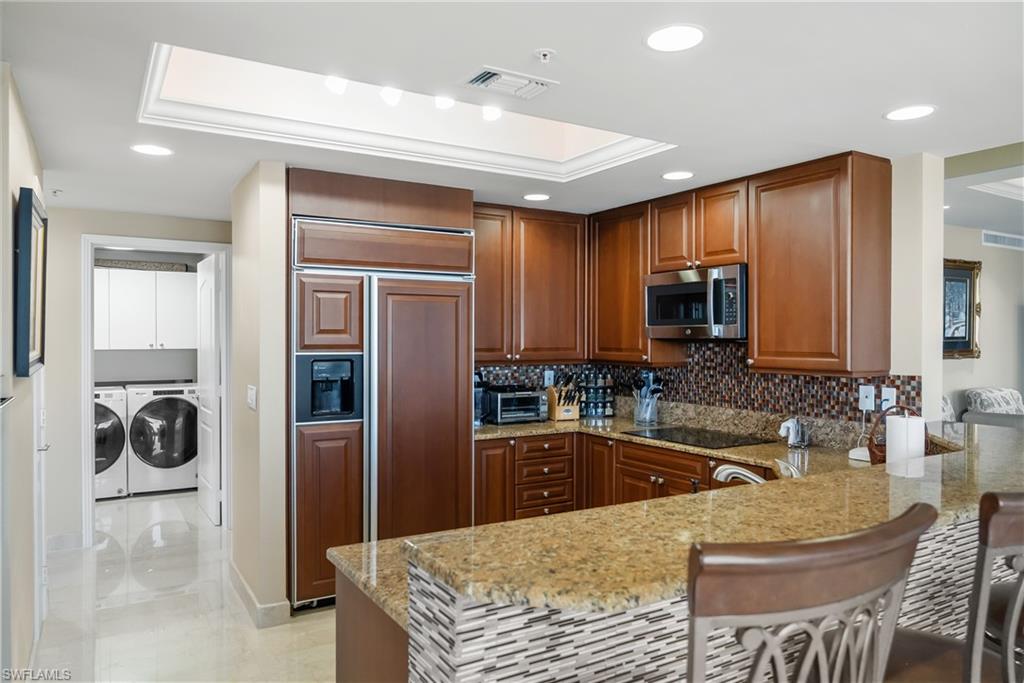 Kitchen featuring wood cabinetry, integrated stainless steel refrigerator, granite countertops, and tile backsplash