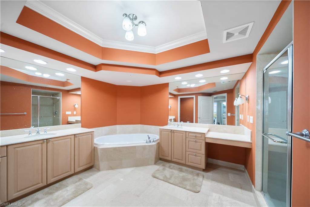 Dual vanity sinks with under-counter cabinetry, a built-in soaking tub, a glass-enclosed shower, and a large wall-mounted mirror