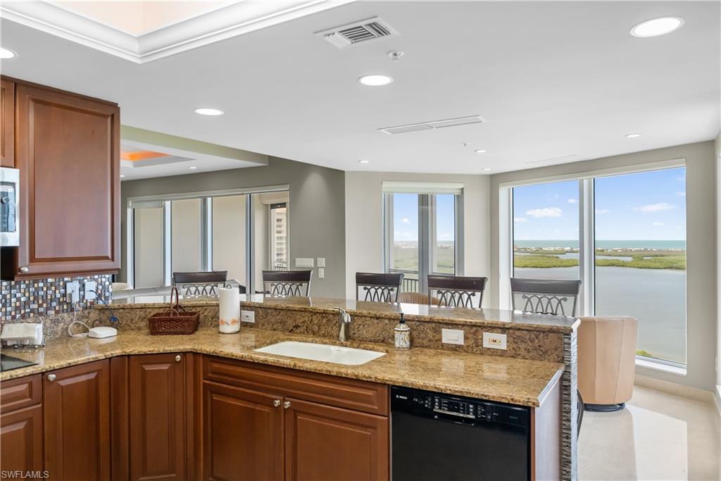 Kitchen featuring wood cabinetry, a built-in dishwasher, and a stone-finish countertop with an integrated sink
