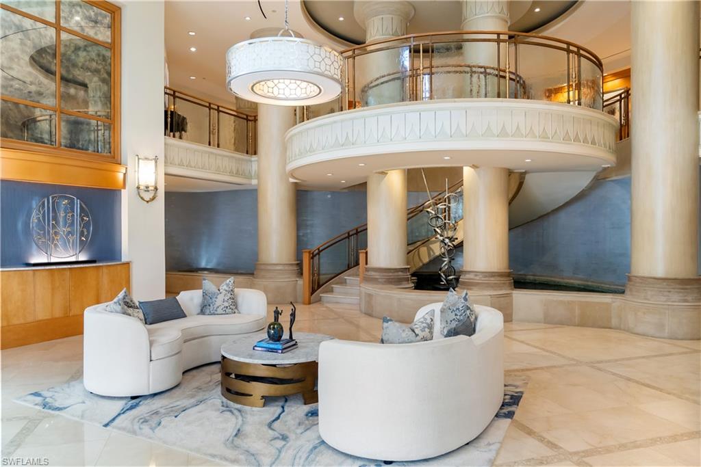 Grand foyer featuring a curved staircase, marble flooring, and decorative columns