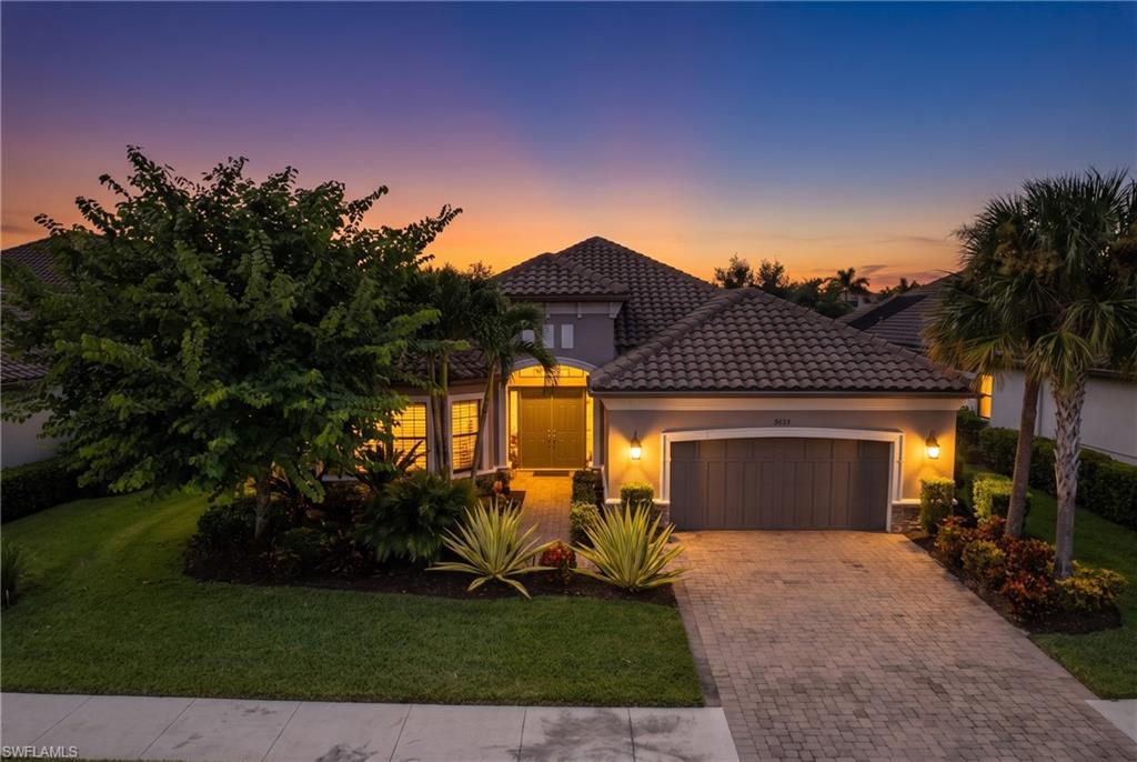 Exterior featuring a paver driveway, illuminated garage door, tiled roof, landscaped front yard, and accent lighting