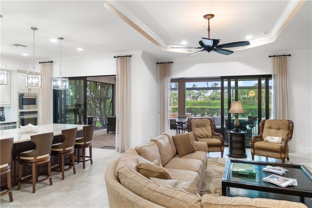 Tray ceiling with a ceiling fan, recessed lighting, expansive sliding glass doors, a large kitchen island with counter seating, and light-toned tile flooring