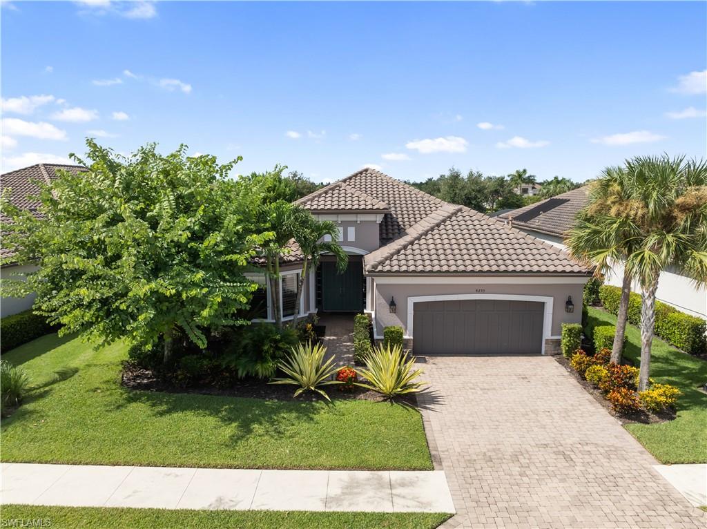 Concrete tile roof, paver driveway, mature landscaping, bay window, and exterior lighting fixtures