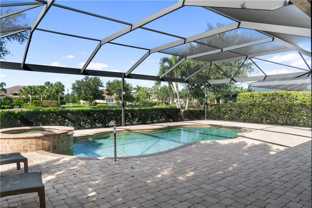 Screened lanai featuring a curved swimming pool, integrated spa with tile surround, and paver patio