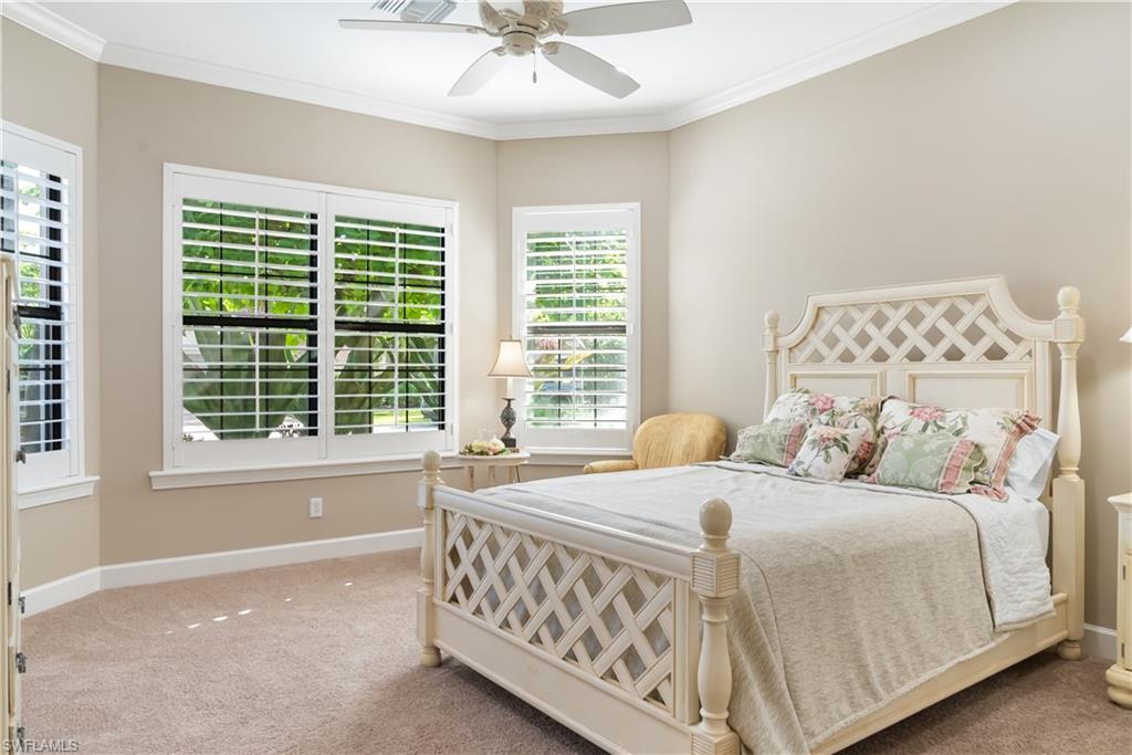 Corner room with multiple windows featuring plantation shutters, crown molding, a ceiling fan, and neutral-toned carpeting