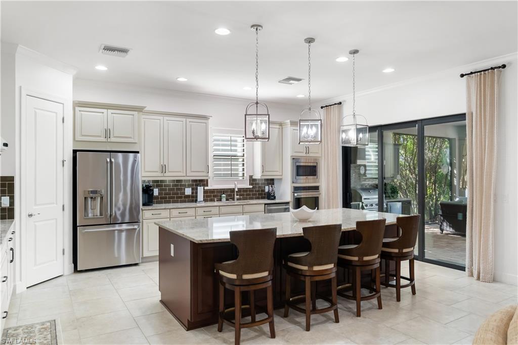 Spacious kitchen featuring an expansive center island, light-toned cabinetry, stainless steel appliances, and large sliding glass doors