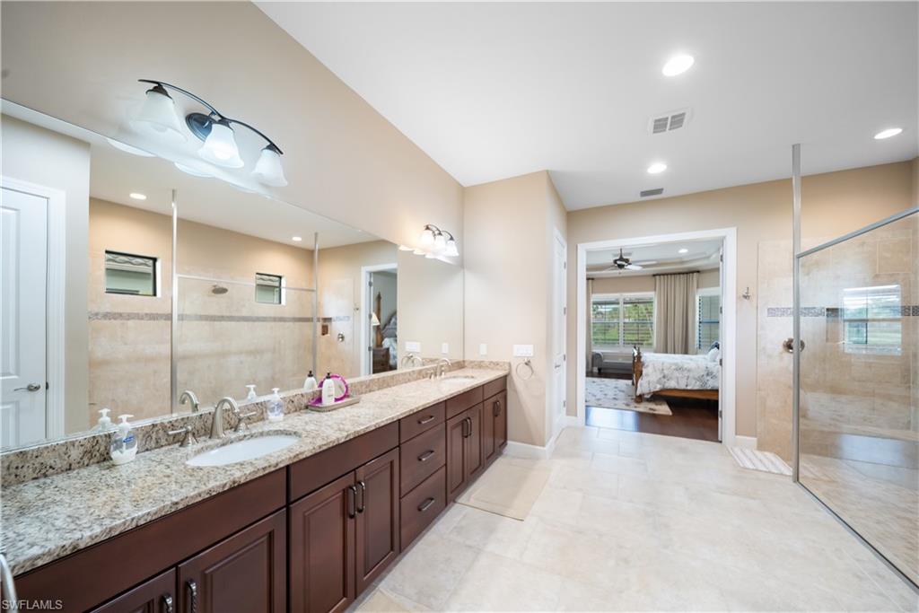 Dual vanity with granite countertops, rich wood-finish cabinetry, and expansive mirror