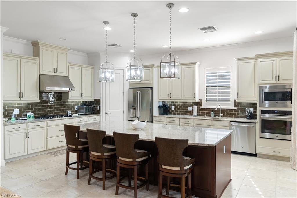 Kitchen featuring a large island, wood cabinetry, built-in stainless steel appliances, a tile backsplash, and overhead pendant lighting