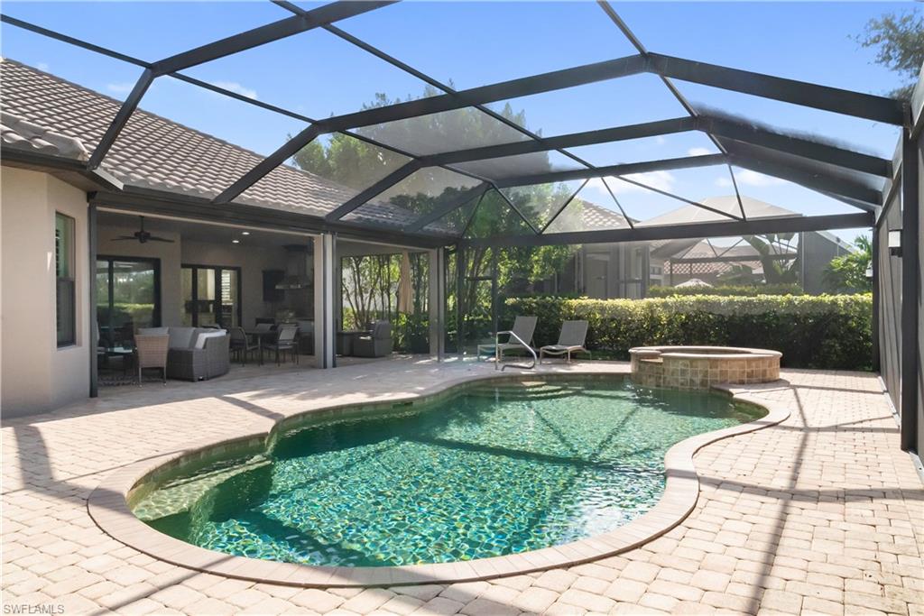 Screened lanai featuring a freeform pool, integrated spa, and extensive paved decking