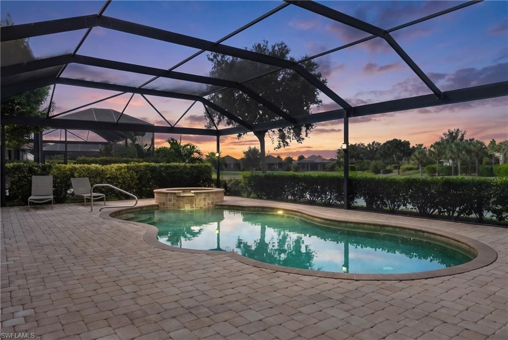 Screened-in outdoor living space featuring a curved swimming pool, integrated spa with stone surround, and paver patio