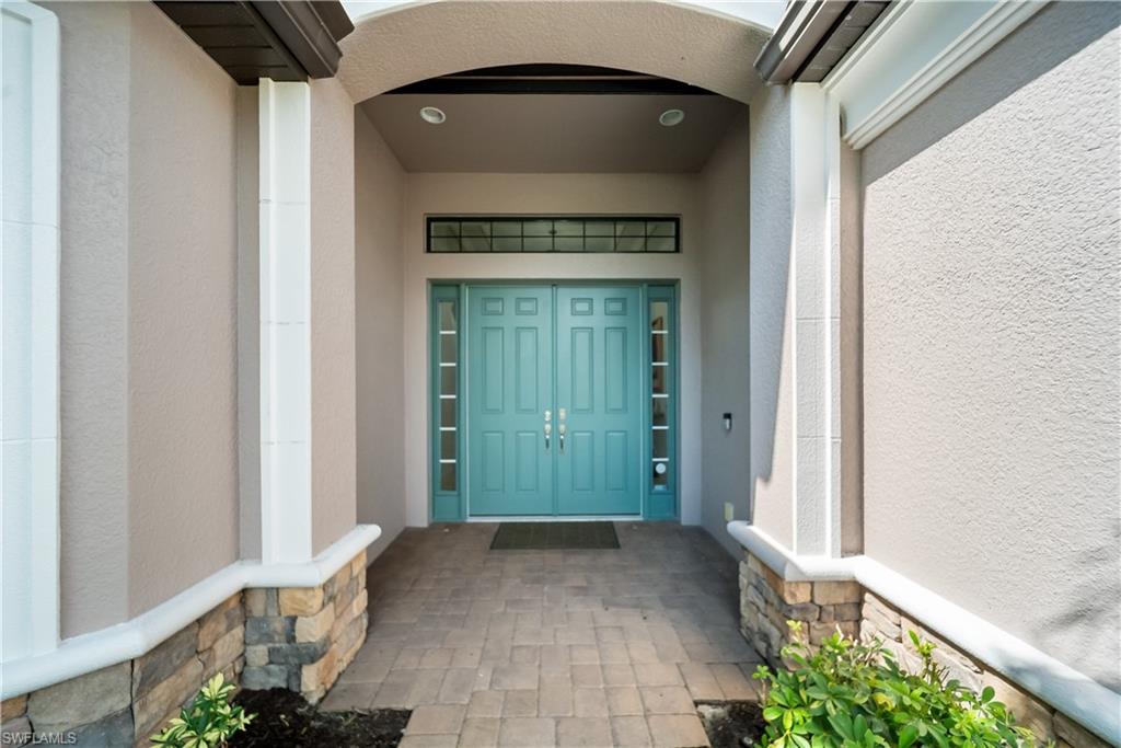 Double entry doors with sidelights and transom window, paver walkway, stucco exterior, and stone veneer accents