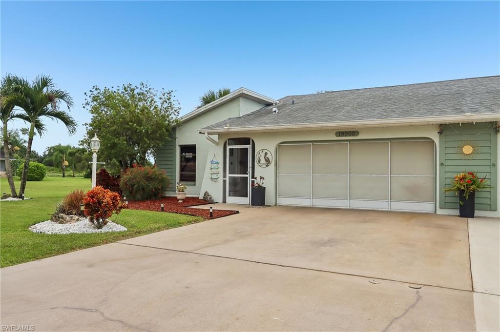 Single-story residence featuring a screened entry, attached garage, concrete driveway, and landscaped front yard with palm trees