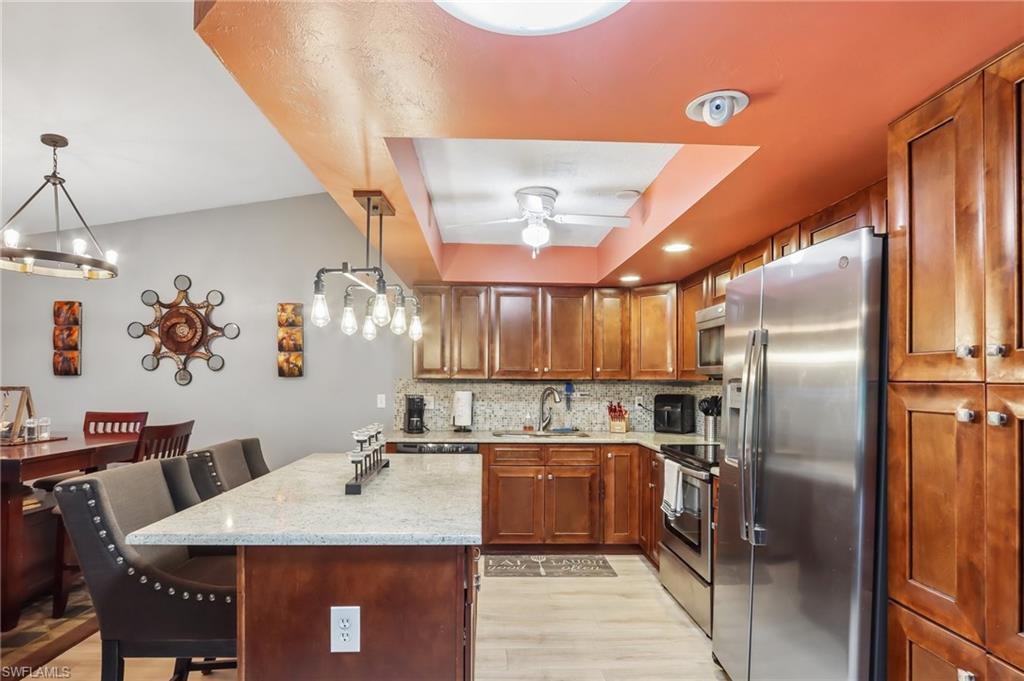 Kitchen featuring wood cabinetry, stainless steel appliances, a light-toned countertop island, and wood-finish flooring