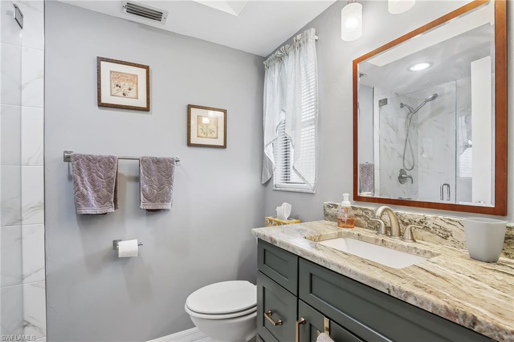 Vanity with integrated sink and stone countertop, wood-framed mirror, built-in cabinetry, and a shower with glass enclosure