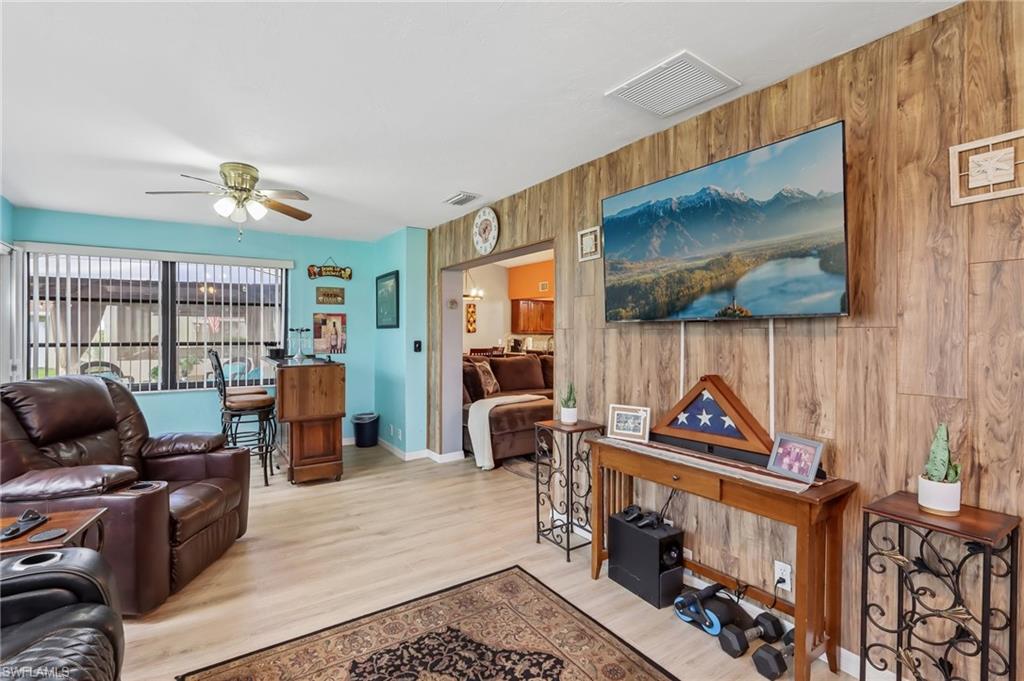 Wood-finish flooring throughout, a wood panel accent wall, and a ceiling fan with integrated lighting