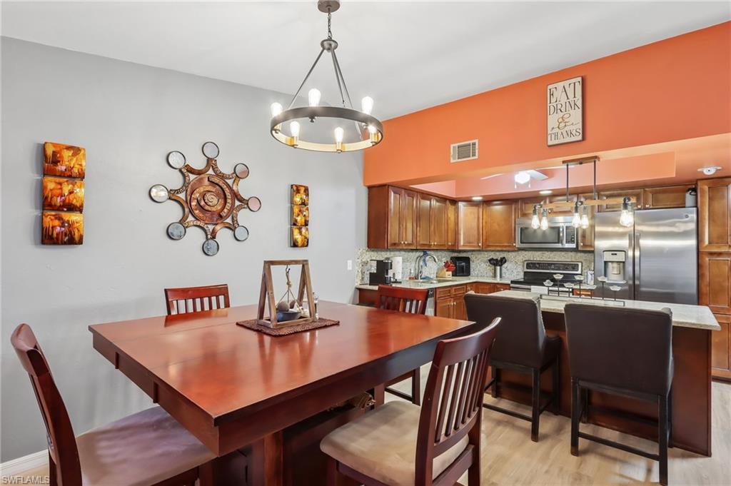 Open-concept kitchen and dining area featuring wood cabinetry, stainless steel appliances, a kitchen island with seating, and a modern chandelier