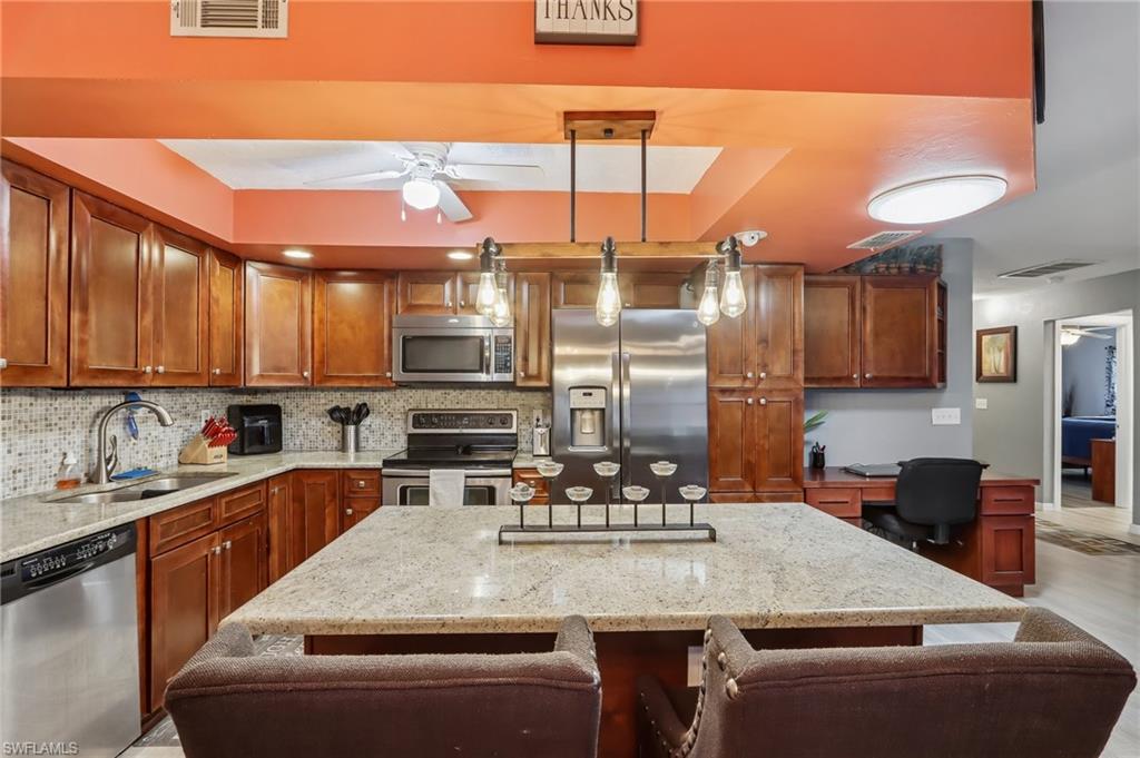 Kitchen featuring wood cabinetry, stainless steel appliances, mosaic tile backsplash, and a large central island with a stone countertop